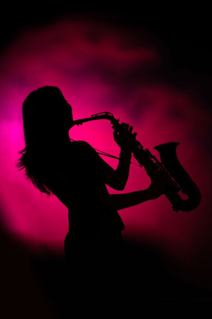 Silhouette of a female saxophonist playing against a vibrant pink background, creating a dramatic musical scene.