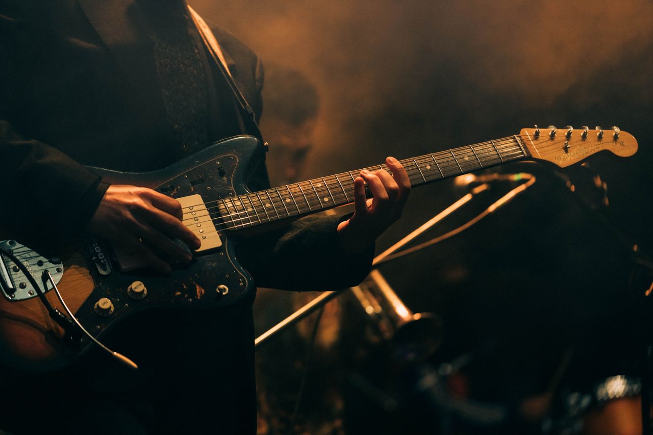 Musician playing electric guitar on stage with dramatic lighting.